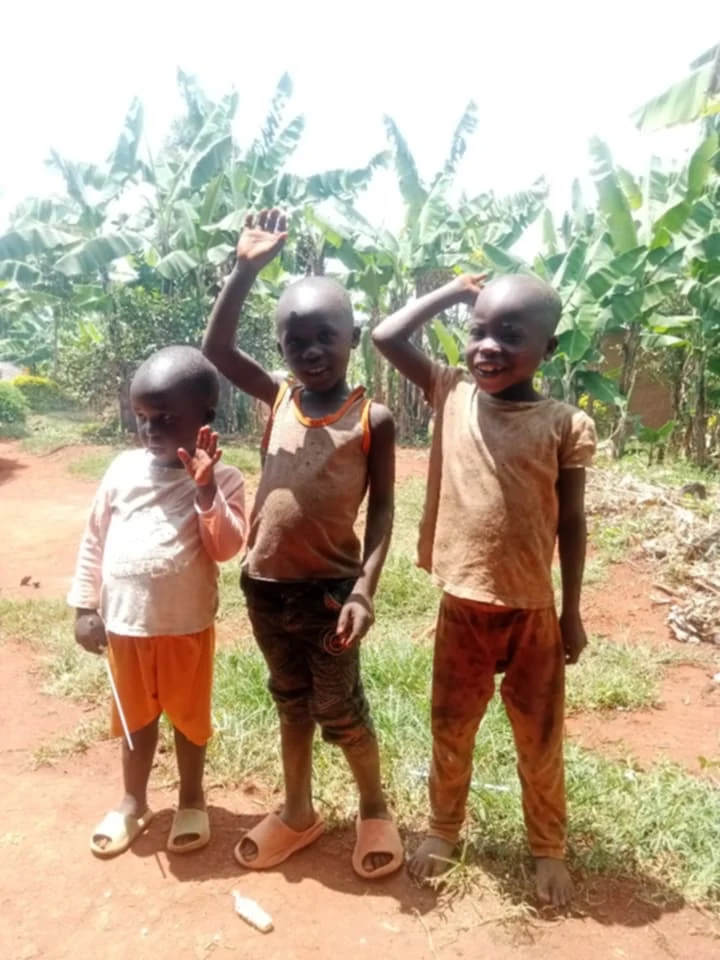 Three children smiling and waving outdoors in Uganda